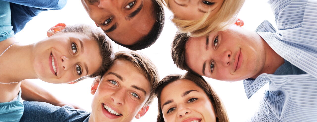 Sechs Personen beugen sich in einem Kreis nach unten. Zwei tragen blaue Hemden, eine Person hat blonde Haare und eine andere braune Haare. Die Gesichter sind teilweise unscharf.