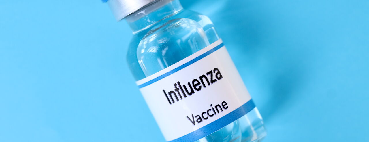 Durchsichtiger Impfstoffbehälter mit silbernem Verschluss und blauer Kappe. Auf dem Etikett steht 'Influenza Vaccine'.