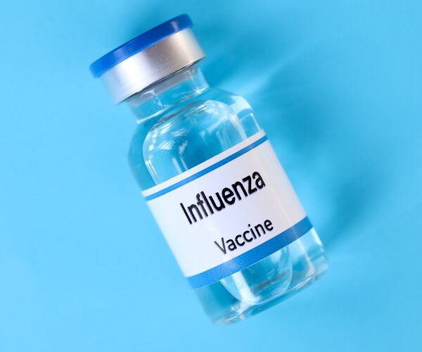 Durchsichtiger Impfstoffbehälter mit silbernem Verschluss und blauer Kappe. Auf dem Etikett steht 'Influenza Vaccine'.